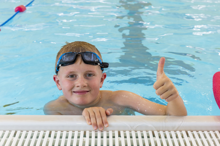 Child at edge of swimming pool with their thumbs up